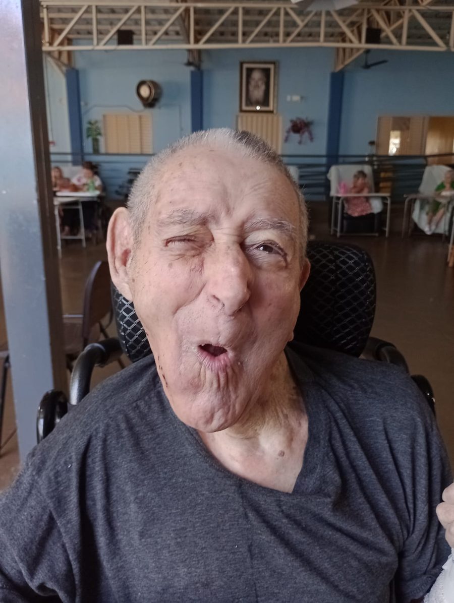 Residente animado durante festa no asilo fazendo expressão bem-humorada na cadeira de rodas